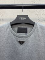T-shirt grigia Prada con logo triangolare e dettagli di alta moda elegante e casual.