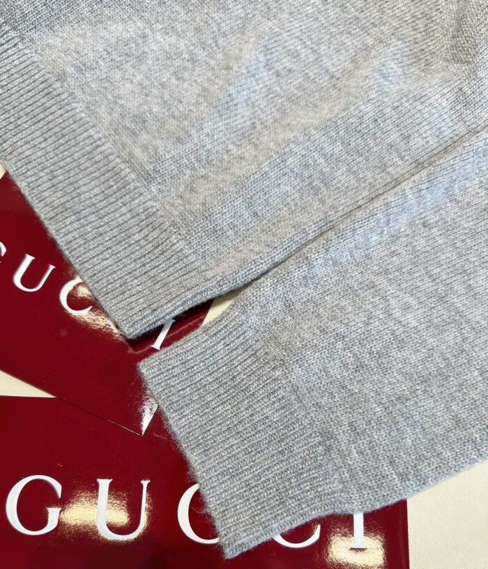 Maglione Gucci grigio di lusso con dettagli raffinati e etichette eleganti rosse.