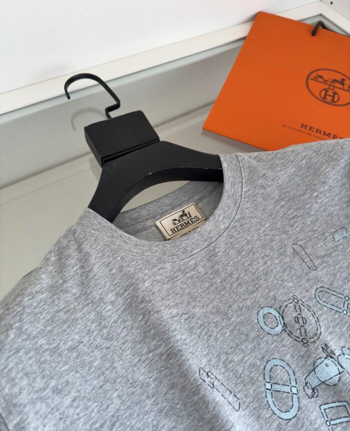 Maglietta grigia di lusso con dettaglio artistico, accompagnata da borsa arancione di marca.