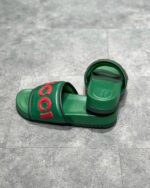 Sandali Gucci verdi con logo rosso, stile moderno, comfort e design di alta qualità.