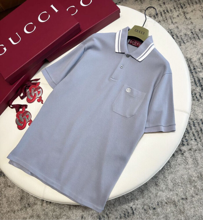 Polo Gucci grigia elegante con dettagli raffinati e confezioni di lusso sullo sfondo.