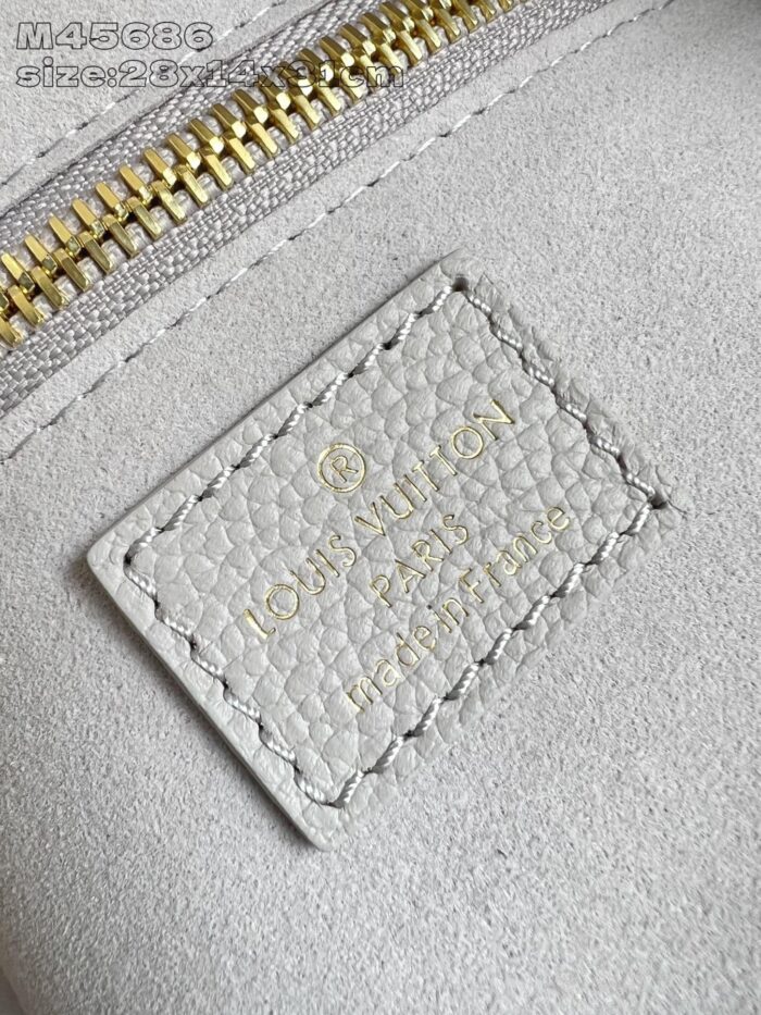 Dettaglio di etichetta Louis Vuitton in pelle grigia con logo dorato e zip elegante.
