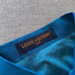 Etichetta Louis Vuitton in blu, dettagli in oro su abito in seta di lusso.