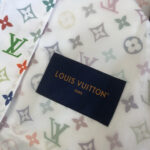Tessuto Louis Vuitton con motivi colorati e etichetta in oro, simbolo di eleganza e lusso.