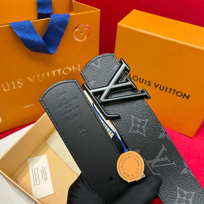 Cintura Louis Vuitton in pelle con logo metallico, accompagnata da shopping bag arancione di lusso.