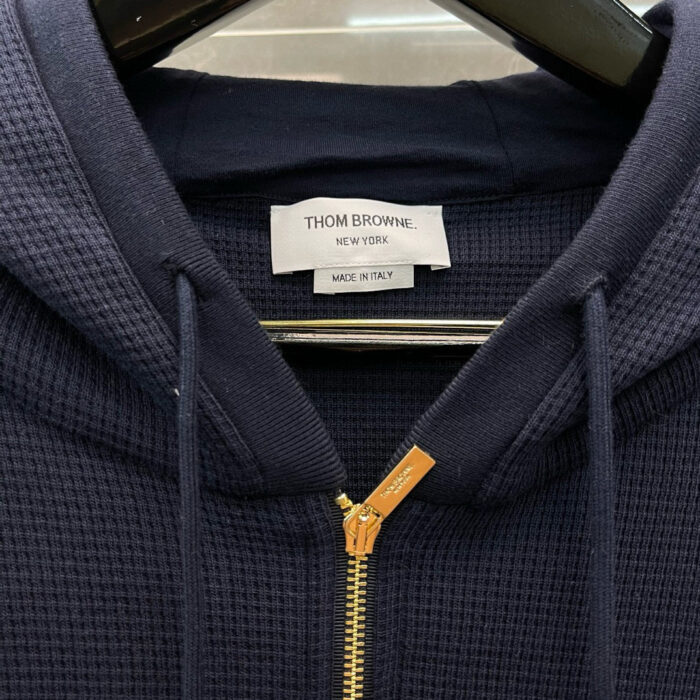 Felpa Thom Browne navy blue, tessuto waffle, zip oro, dettagli eleganti, made in Italy.