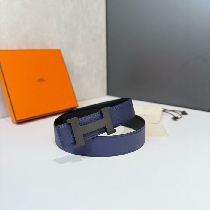 Cintura di lusso in pelle navy con fibbia a forma di H e packaging elegante.