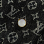 Bottone in metallo iridescente su jeans con logo Louis Vuitton, simbolo di lusso e stile.