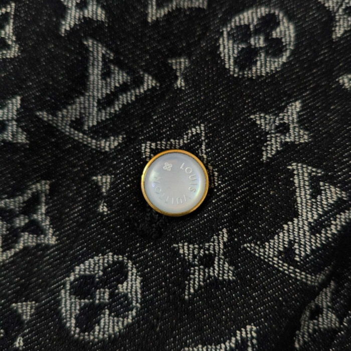 Bottone in metallo iridescente su jeans con logo Louis Vuitton, simbolo di lusso e stile.