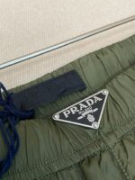 Pantaloni Prada verde oliva con logo in metallo, dettagli eleganti e stile casual sofisticato.