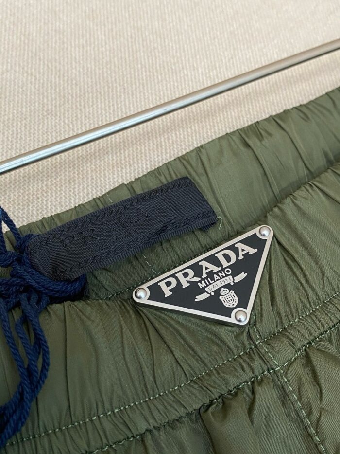 Pantaloni Prada verde oliva con logo in metallo, dettagli eleganti e stile casual sofisticato.