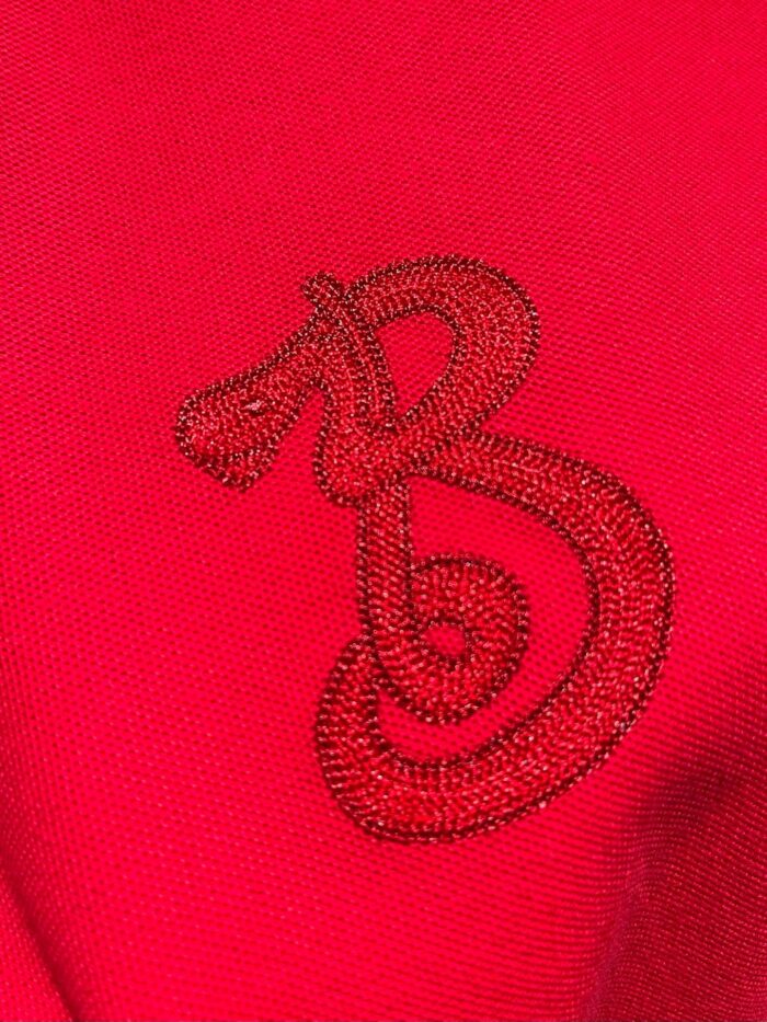 Emblema elegante ricamato su tessuto rosso intenso, stile logo animale e lettera B.