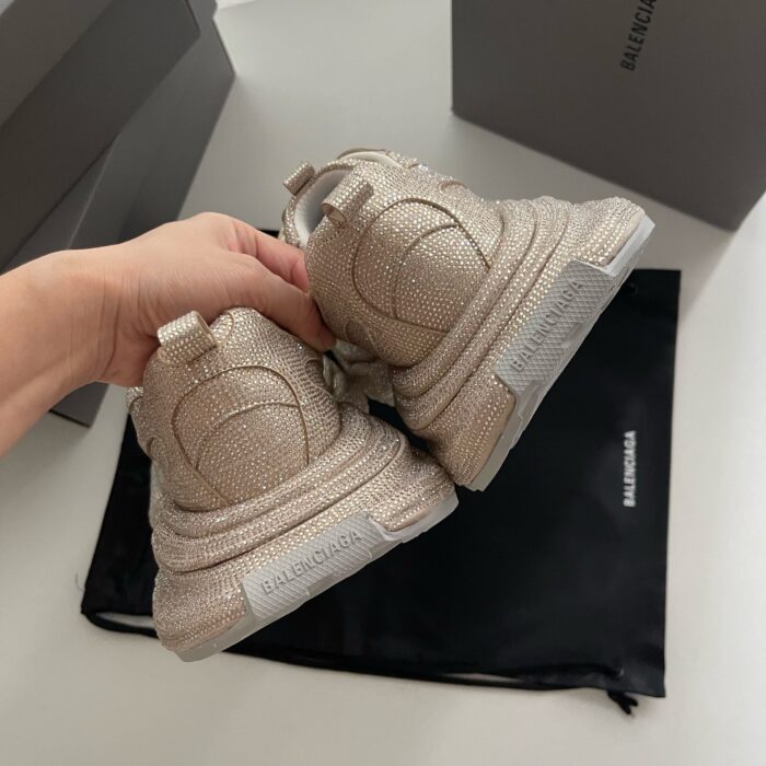 Sneaker di lusso beige con dettagli shimmer, packaging elegante e dust bag, stile raffinato.