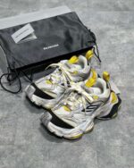Sneakers Balenciaga bianche con dettagli gialli e neri, stile moderno e luxury.