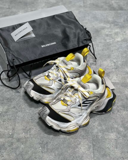Sneakers Balenciaga bianche con dettagli gialli e neri, stile moderno e luxury.