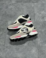 Sneakers di lusso beige, nero e rosa con design sportivo, logo distintivo e dettagli moderni.
