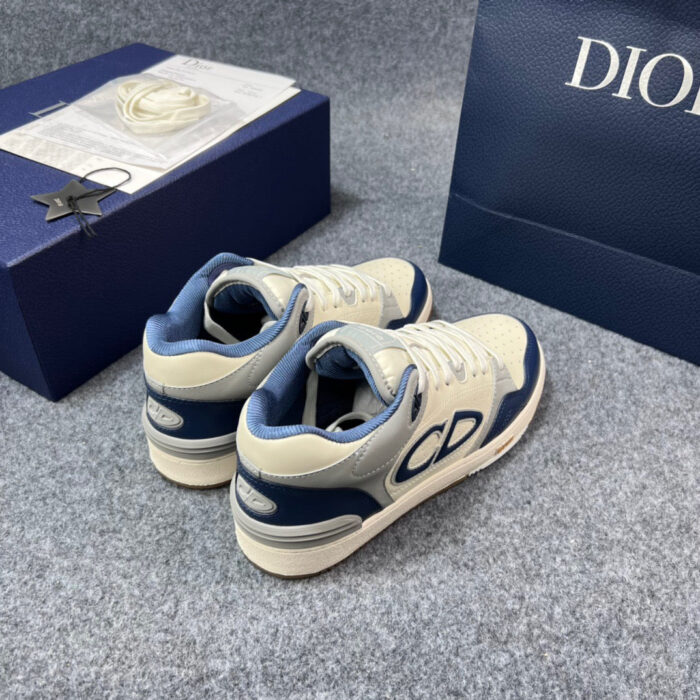Sneakers di lusso crema e navy con logo CD e scatola elegante su sfondo grigio.