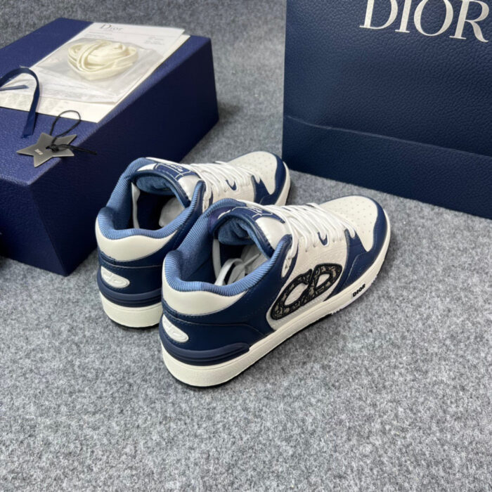 Sneakers di lusso bianche con dettagli navy, presentate con elegante scatola regalo blu raffinata.