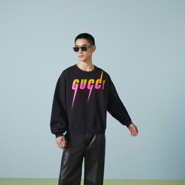 Modello con felpa Gucci, pantaloni in pelle e occhiali da sole trendy, stile casual elegante.