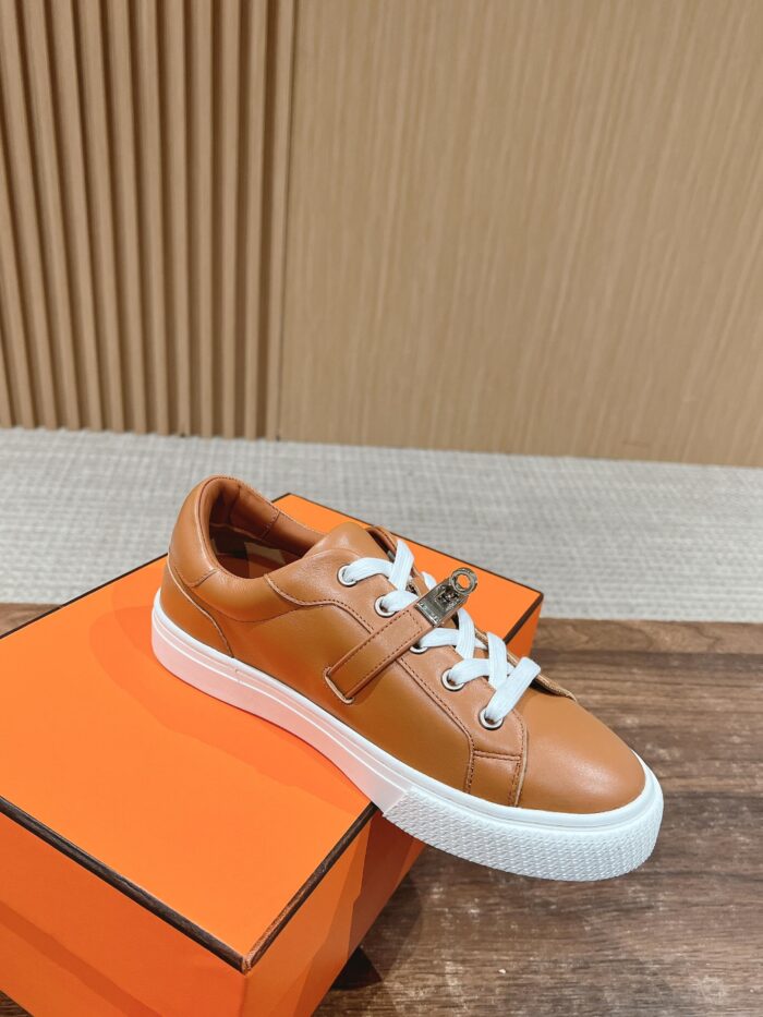 Sneaker in pelle tan minimalista con dettagli metallizzati su scatola arancione elegante.