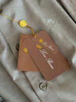 Abbigliamento di moda beige con etichette di lusso e bottoni eleganti, perfetto per uno stile raffinato.