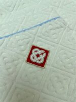 Asciugamano di lusso con logo ricamato rosso e dettaglio blu decorativo.