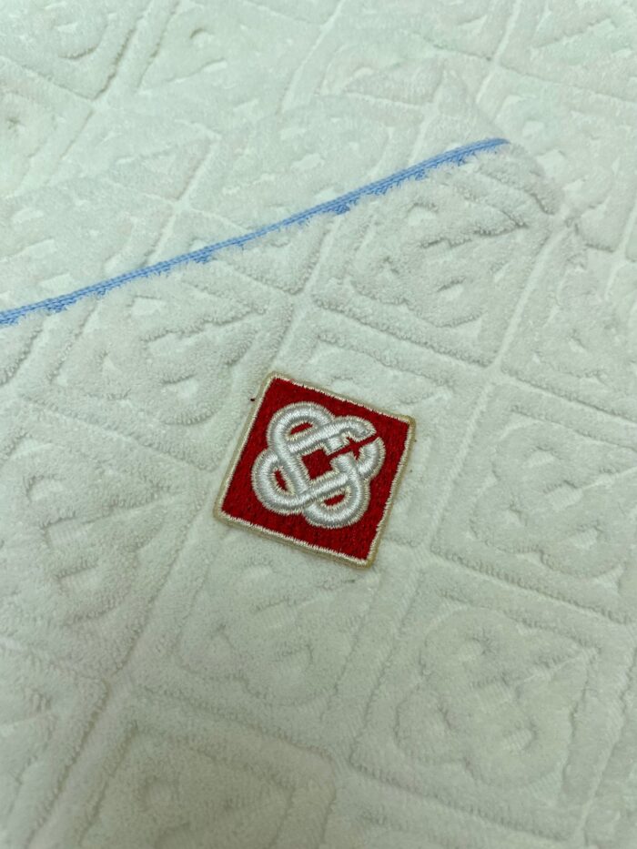 Asciugamano di lusso con logo ricamato rosso e dettaglio blu decorativo.