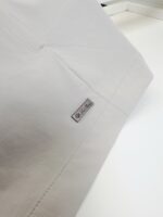 Tessuto bianco di alta qualità con tag metallico elegante e cuciture precise.