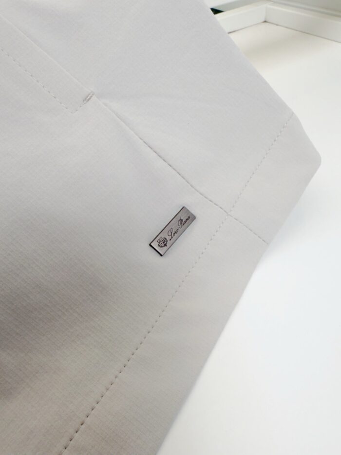 Tessuto bianco di alta qualità con tag metallico elegante e cuciture precise.
