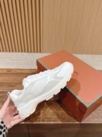 Sneaker bianca di lusso con suola spessa e packaging elegante su superficie in legno.