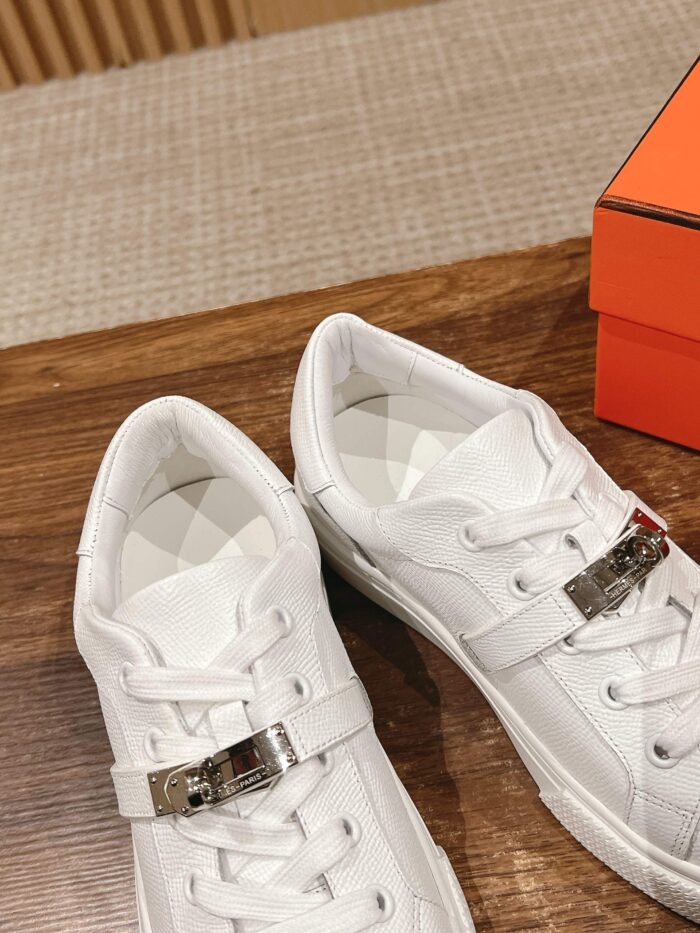 Sneaker bianca di lusso in pelle con fibbia argento su superficie in legno elegante.