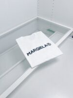 Maglia bianca Margiela minimalista su superficie in vetro, stile elegante e sofisticato.
