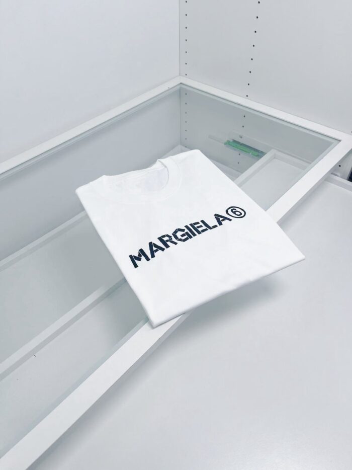 Maglia bianca Margiela minimalista su superficie in vetro, stile elegante e sofisticato.
