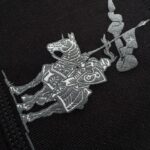 Cavaliere in armatura con cavallo, ricamo grigio su sfondo nero, simbolo di valore e coraggio.