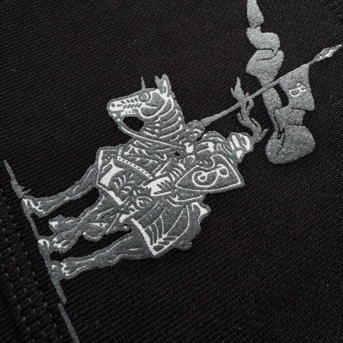 Cavaliere in armatura con cavallo, ricamo grigio su sfondo nero, simbolo di valore e coraggio.