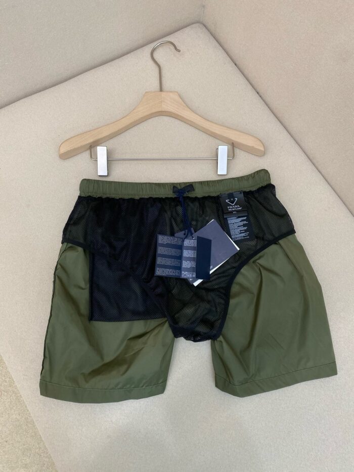 Pantaloncini sportivi verdi oliva con mesh, elastico in vita e cordino blu, perfetti per attività outdoor.