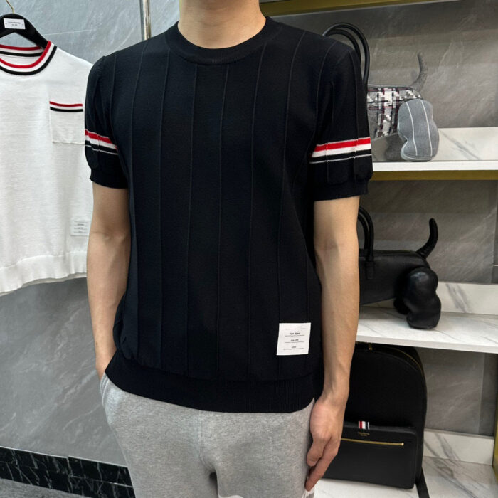 Uomo con maglione nero a righe rosse e pantaloni grigi, stile casual e moderno.