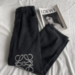 Jeans neri con logo artistico e magazine Loewe su sfondo minimalista.