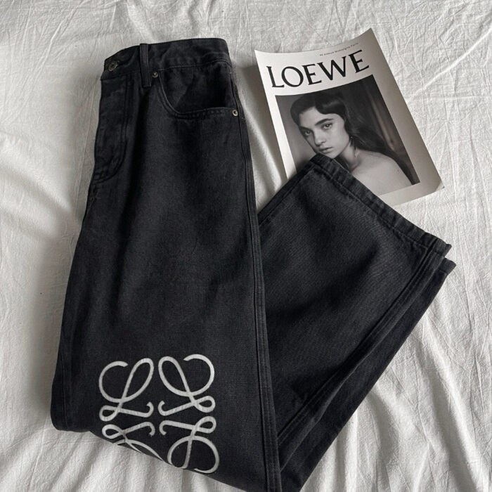 Jeans neri con logo artistico e magazine Loewe su sfondo minimalista.