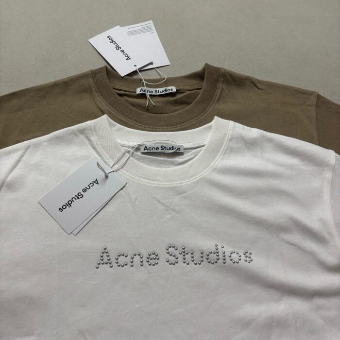 T-shirt Acne Studios beige e bianco con logo ricamato, stile minimalista e moderno.