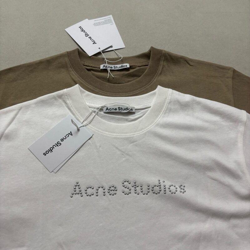 T-shirt Acne Studios beige e bianco con logo ricamato, stile minimalista e moderno.