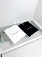 T-shirt minimaliste bianca e nera in esposizione elegante su superficie bianca.
