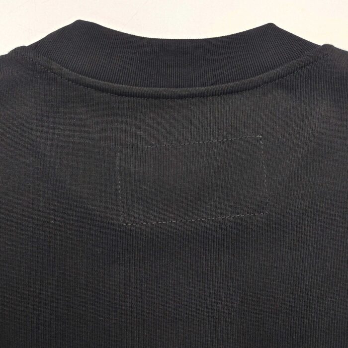 Maglietta nera minimalista con collo a coste e dettaglio rettangolare senza logo.