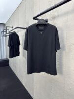 Magliette nere minimaliste su asta in ambiente moderno con parete in cemento e luce naturale.