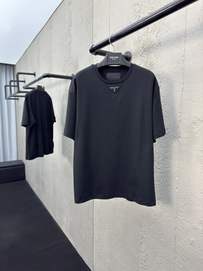 Magliette nere minimaliste su asta in ambiente moderno con parete in cemento e luce naturale.