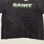 T-shirt nero casual con testo SAINT verde e bianco, stile streetwear, look urbano e informale.