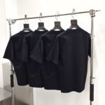 Set di quattro magliette nere minimaliste su appendino moderno in metallo lucido.