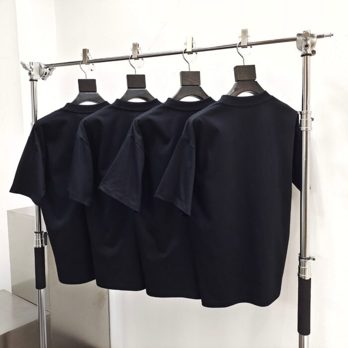 Set di quattro magliette nere minimaliste su appendino moderno in metallo lucido.