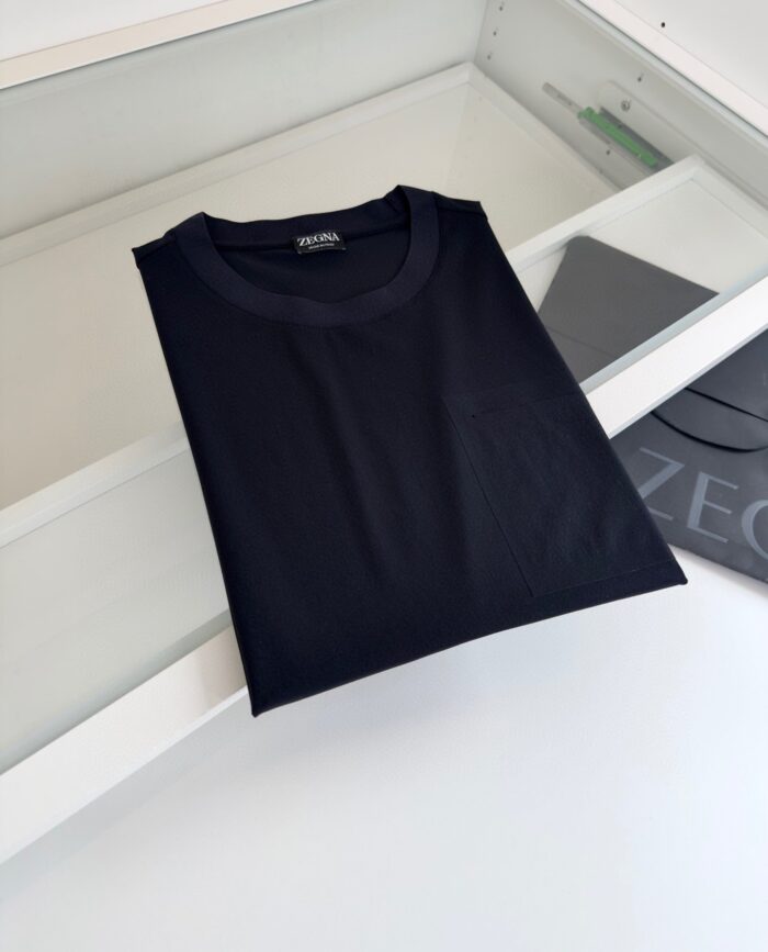 Maglietta nera minimalista piegata su superficie chiara in ambiente moderno ed elegante.
