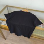 Maglietta nera casual, semplice e versatile su tavolo di vetro e legno, stile minimalista.